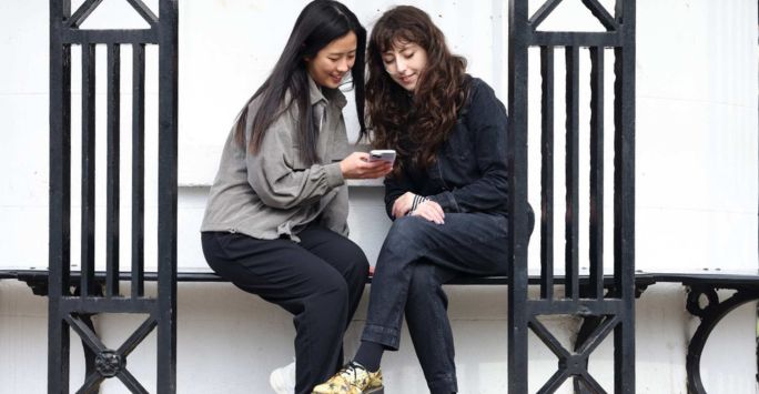 2 women students sitting on a bench on campus