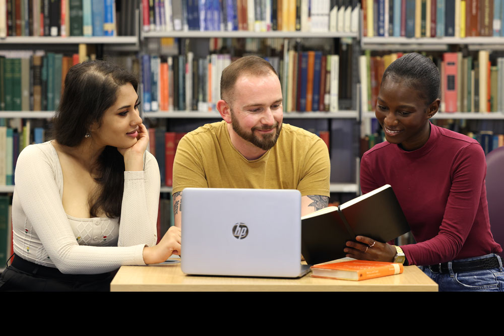 Three students in a library looking at a laptop