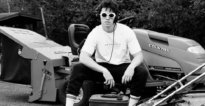 black and white image of a young man in sunglasses sitting on machinery
