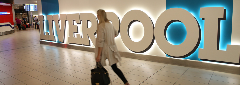 A woman carrying a bag walks past a large Liverpool sign.
