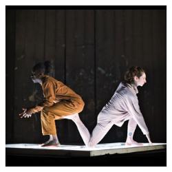 Two dancers facing away from each other against a dark background