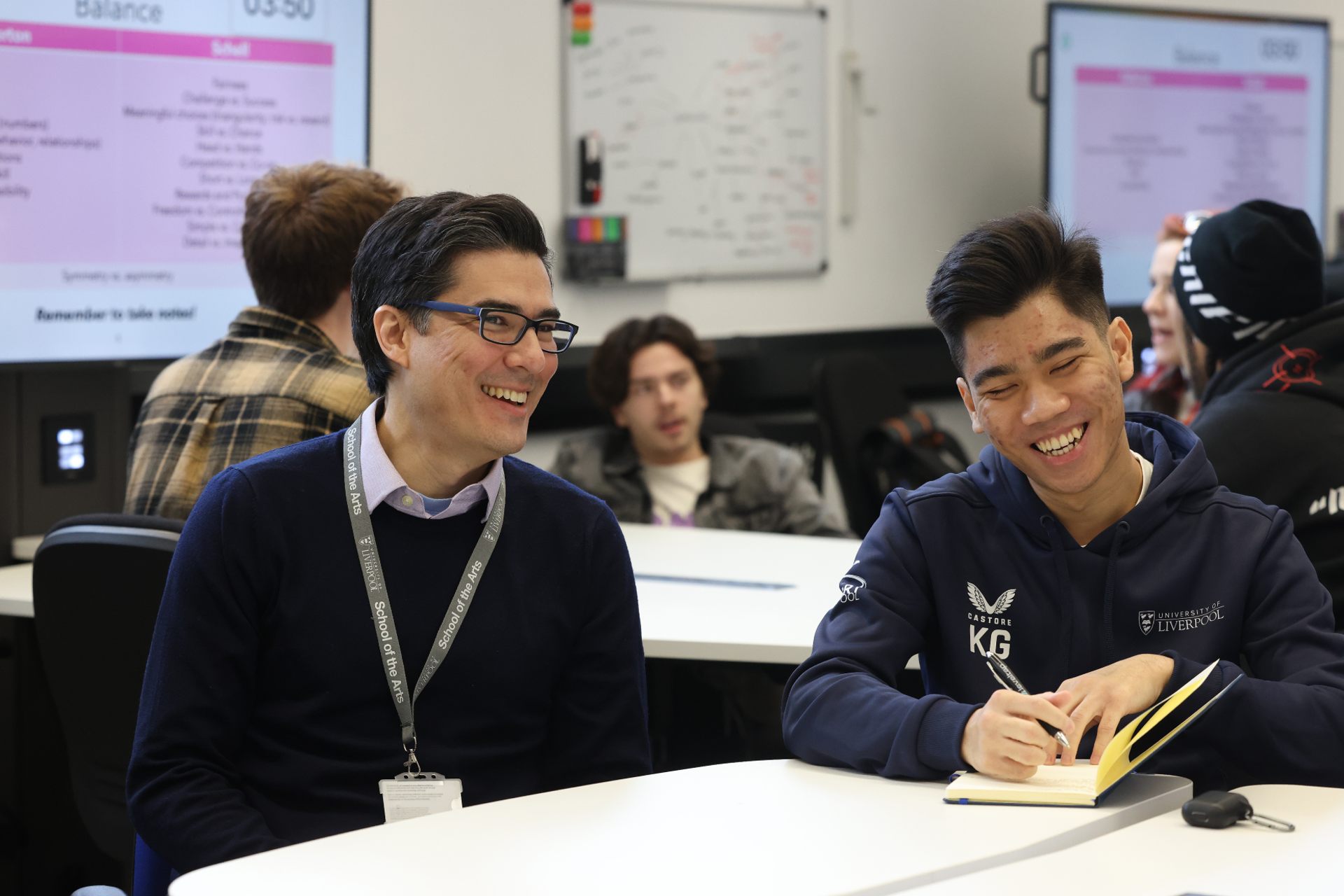 A student and member of staff sitting together, talking and smiling.