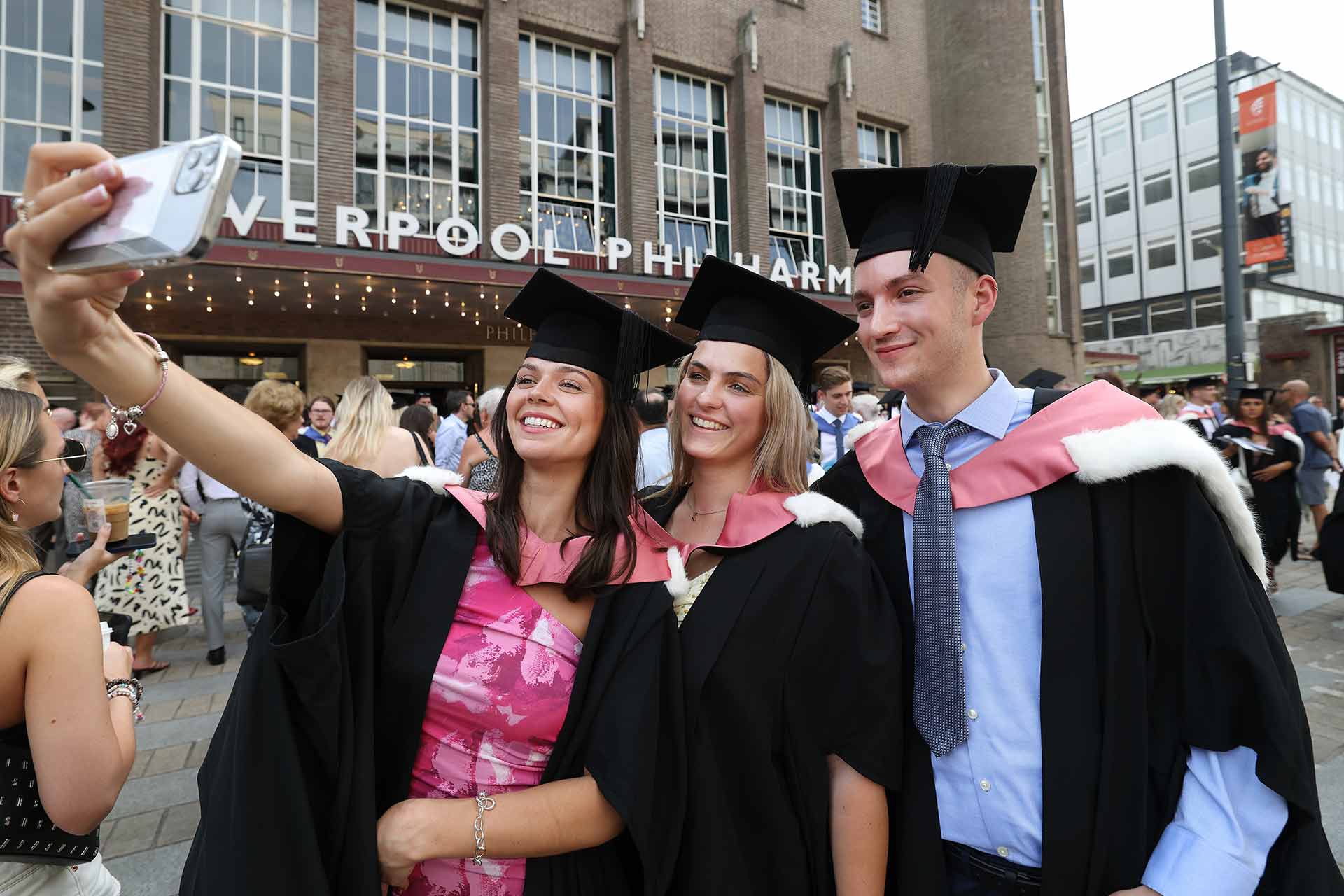Three graduates pose for a selfie outside the Liverpool Philharmonic Hall on their graduation day.