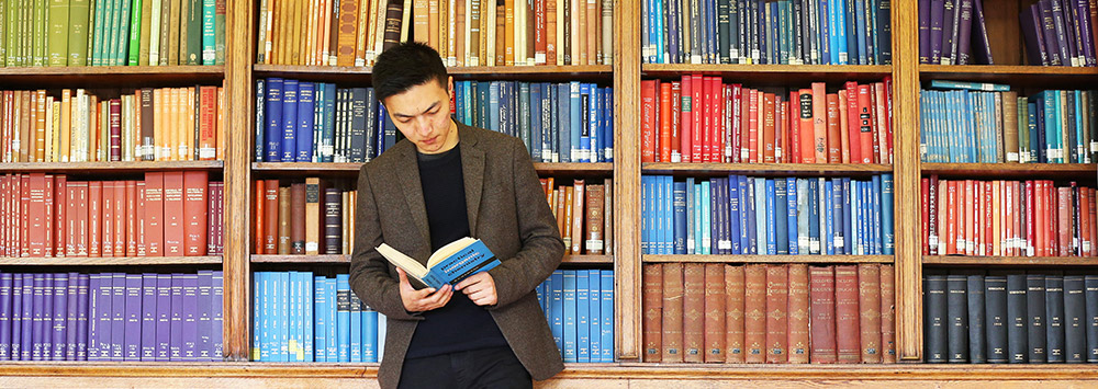 Student reading in front of a bookshelf full of colourful books