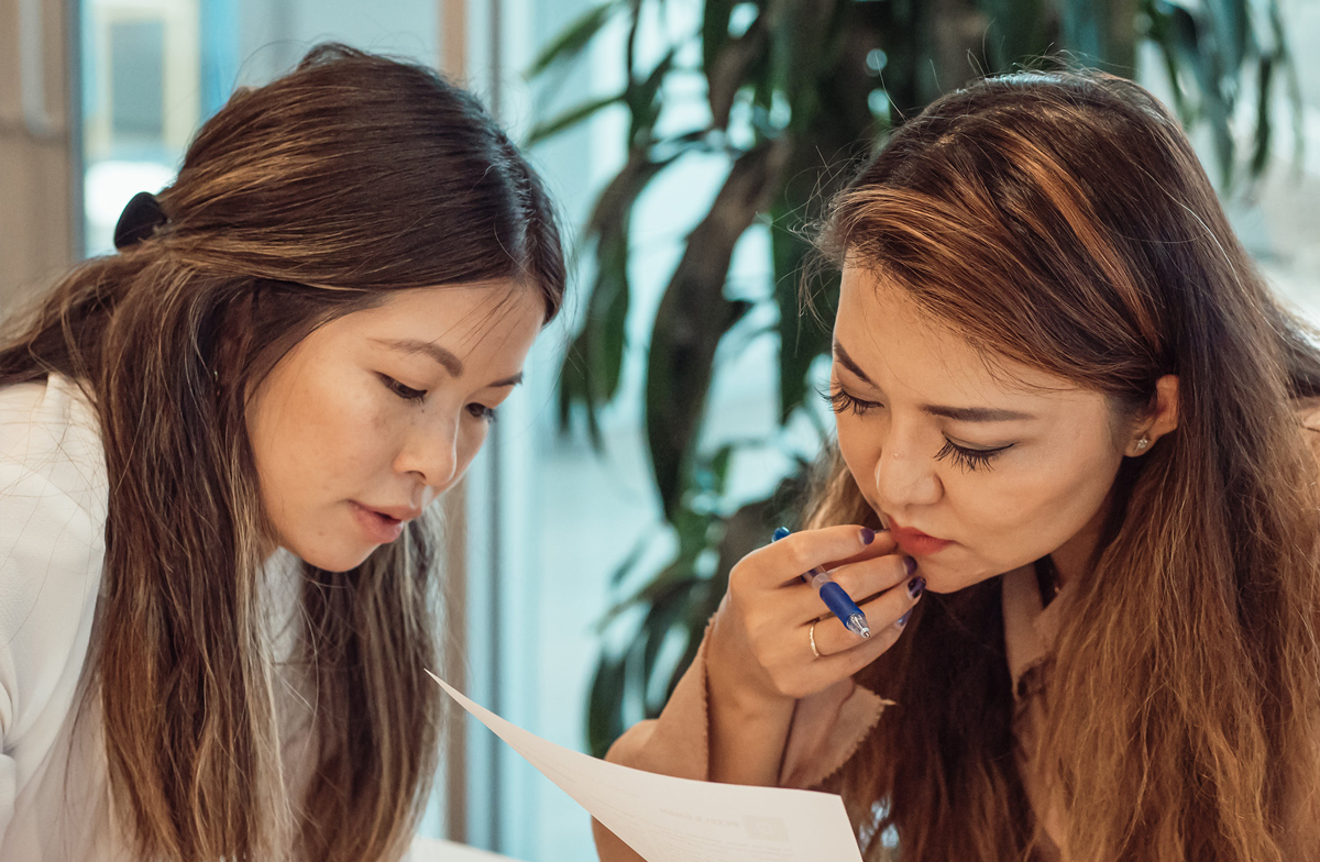 An image of two people reading the same piece of paper, one has a pen in their hand.