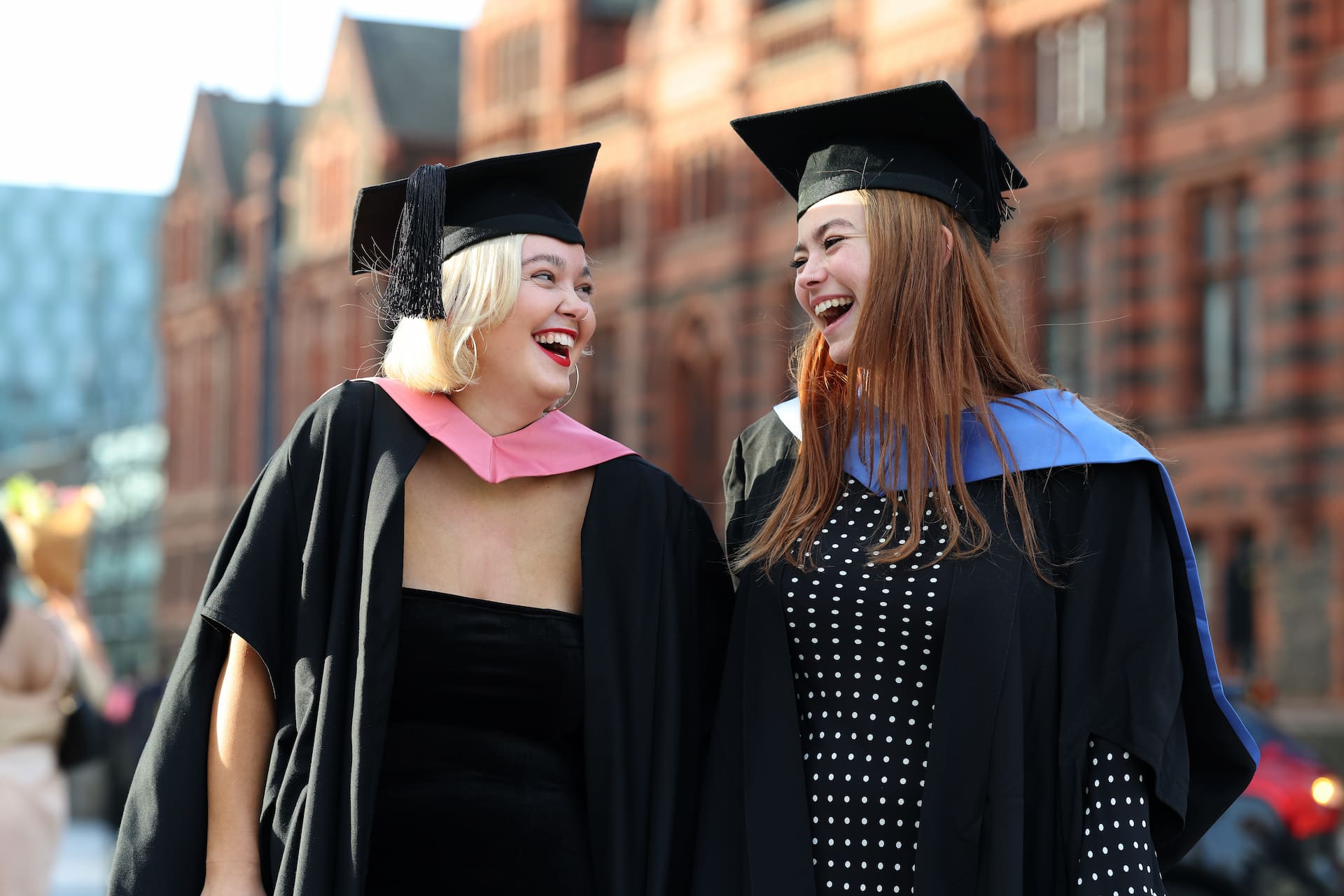 Two students in gowns and gaps smile at each other