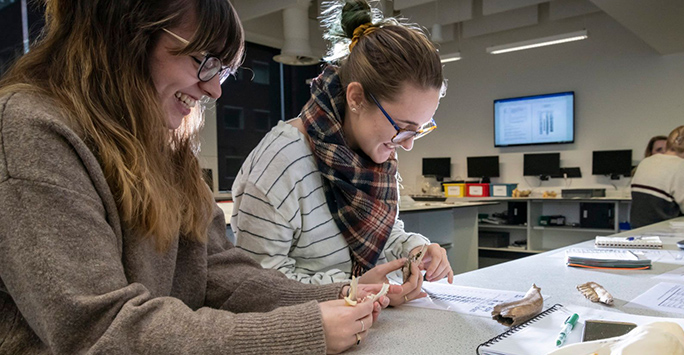 Two students examining bone fragments in an archaeology laboratory.