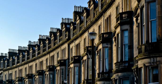 A close-up photograph of the upper floors of a curved row of grand terraced houses. There is a blue sky in the background.