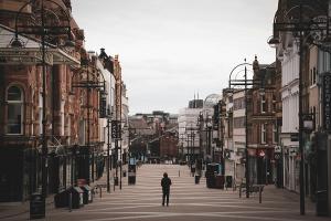 A single person is walking down a wide and otherwise empty high street.