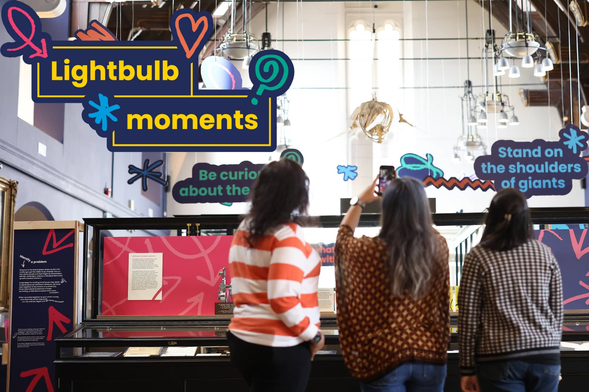Three people looking at the Lightbulb moments exhibition in the Tate Hall in the Victoria Gallery and Museum