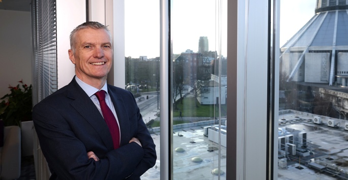 man standing with folded arms next to window