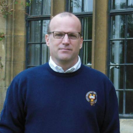 man in glasses and navy jumper standing outside building