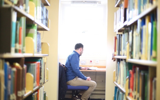 A student works at the end of a row of books at the library.