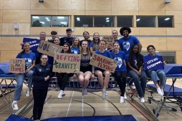 Members of the trampolining club holding signs and smiling