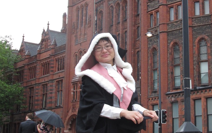 PhD student Xinxin Cao wearing graduation robes in front of the Victoria Building.