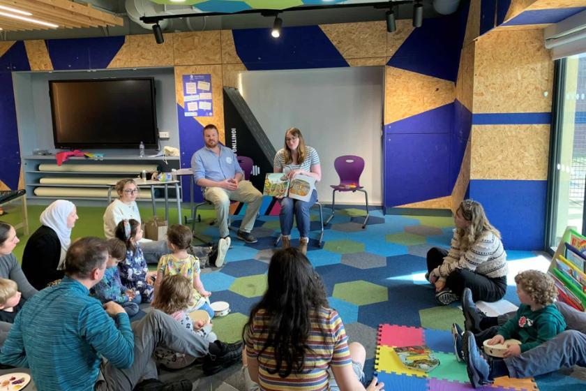 Toddlers in a classroom with teacher at the front holding a picture book