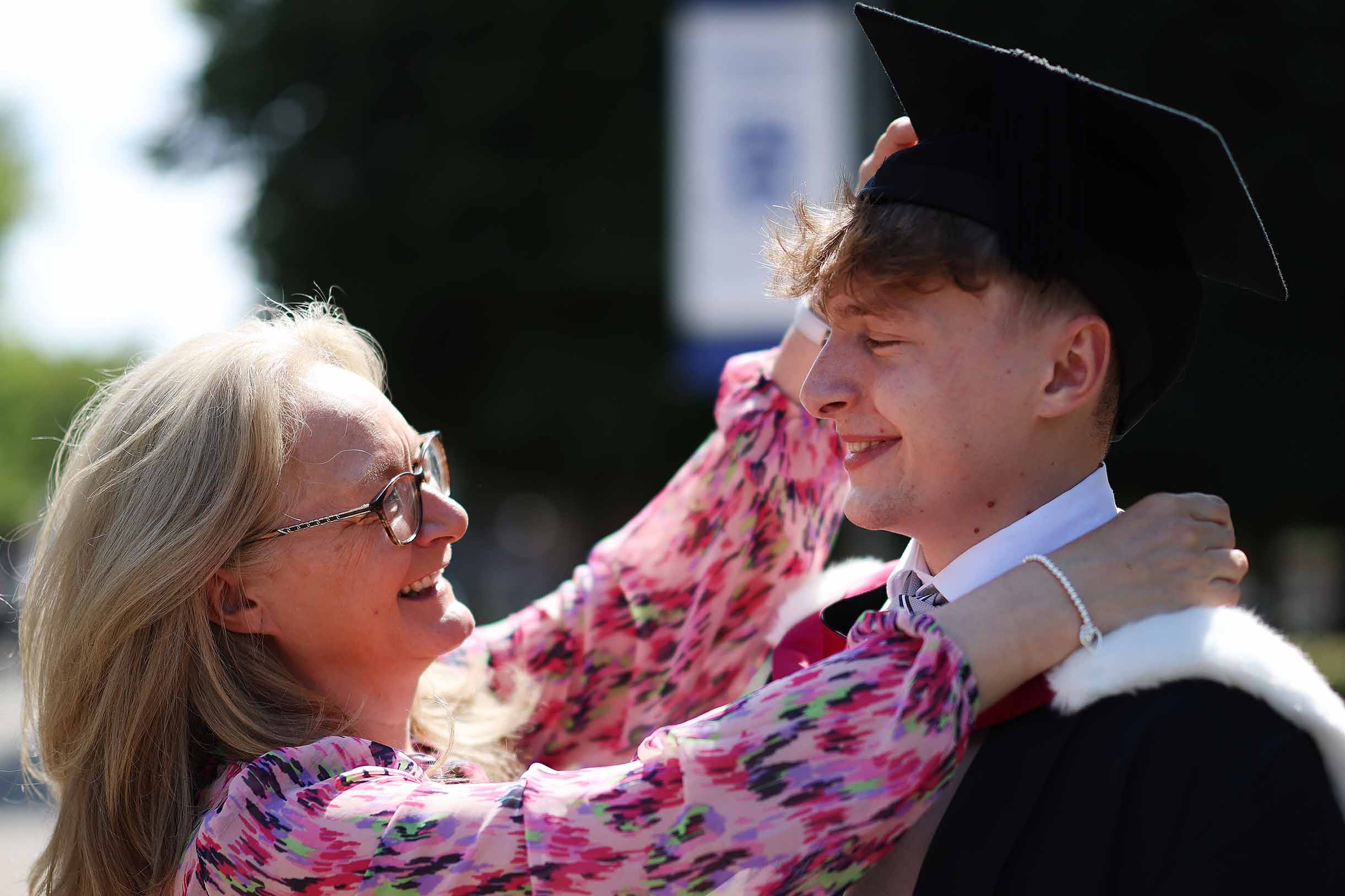 Two people with one person fixing the others graduation cap and gown