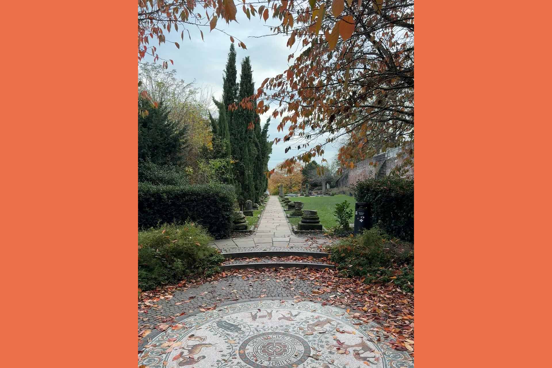 A garden in autumn, with hedges and trees in the background and a circular stone paving stone in the foreground