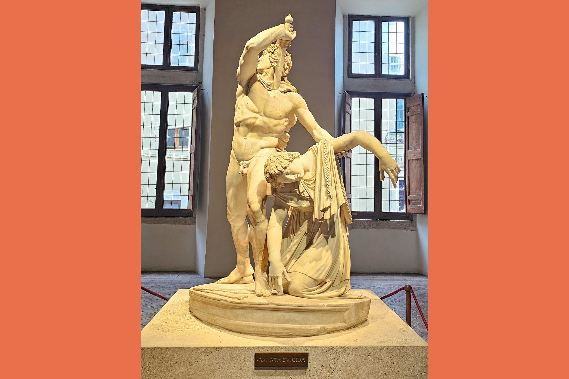 An old marble statue of a man wiedling a large sword to himself in his right hand and holding up another person who has collapsed in his left hand.