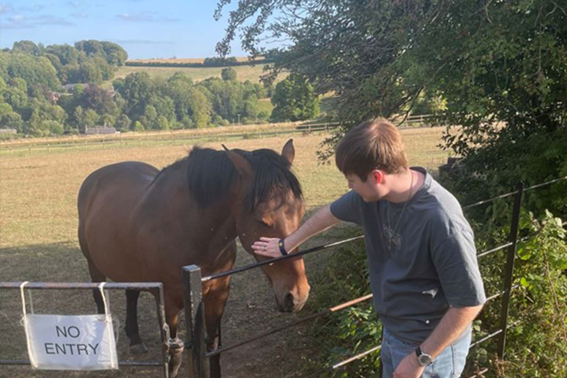 A young man stroking a horse on it's head in the countryside