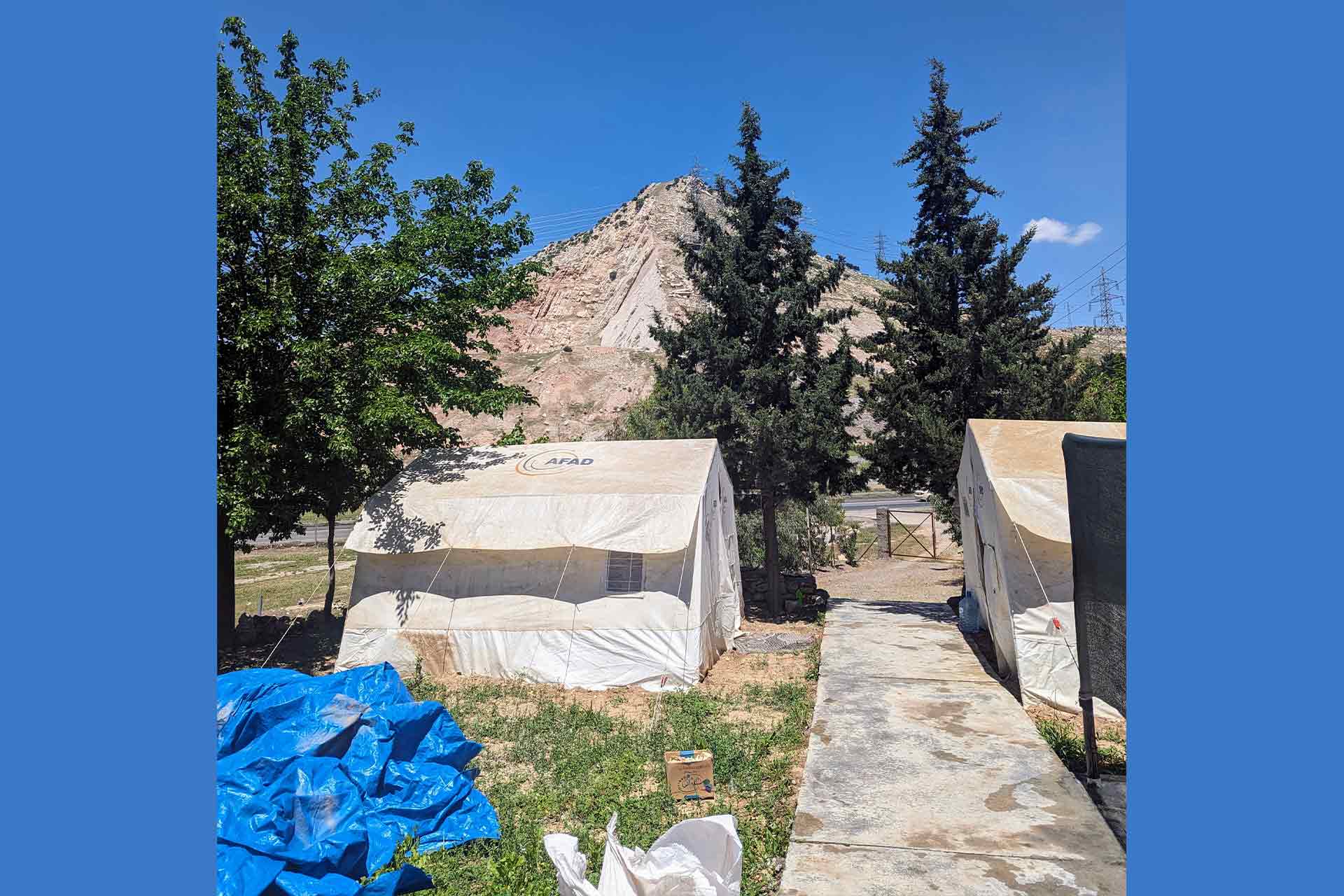 Outdoor excavation area with archaeological tents in the foreground with trees and a sandy hill in the background