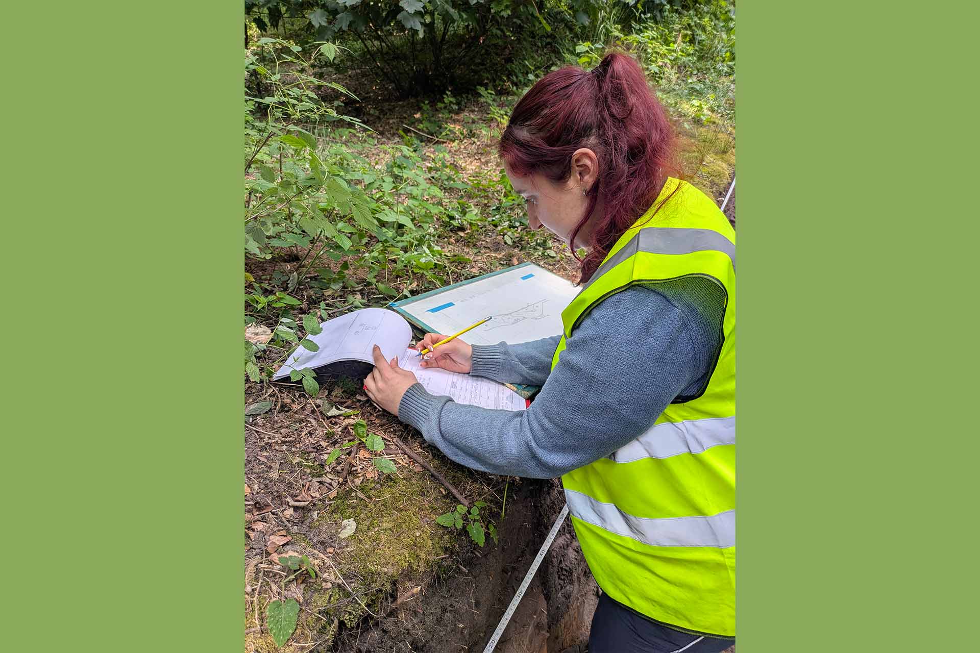 A student wearing a high-vis outside writing on a piece of paper.