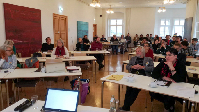 Room of conference attendees sat at desks at the panel event in Graz