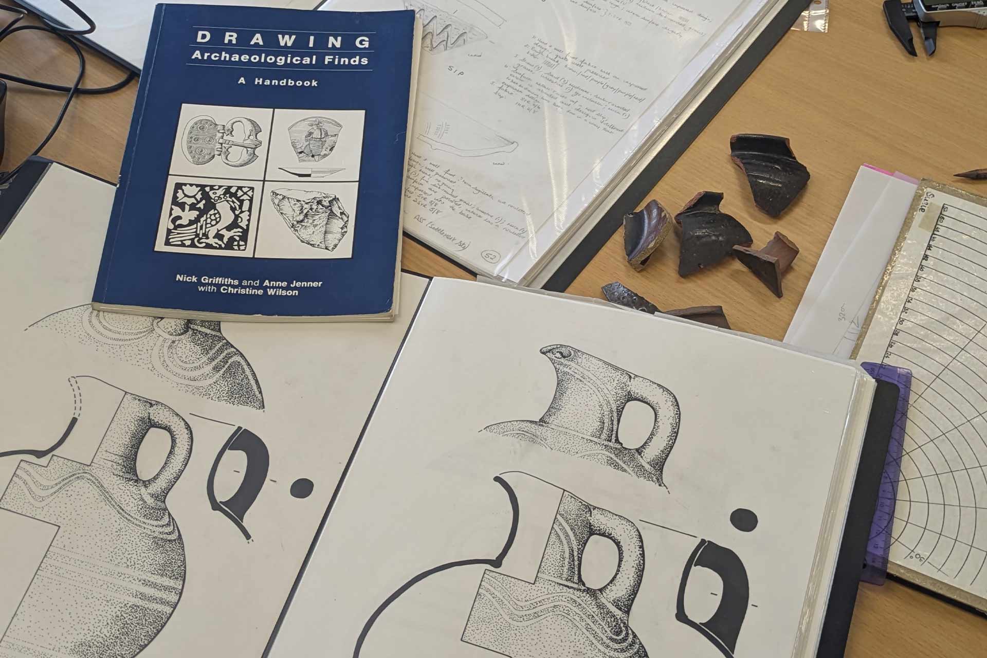 A portfolio of archaeology drawings and a book 'Drawing Archaeological Finds - a handbook' on a table