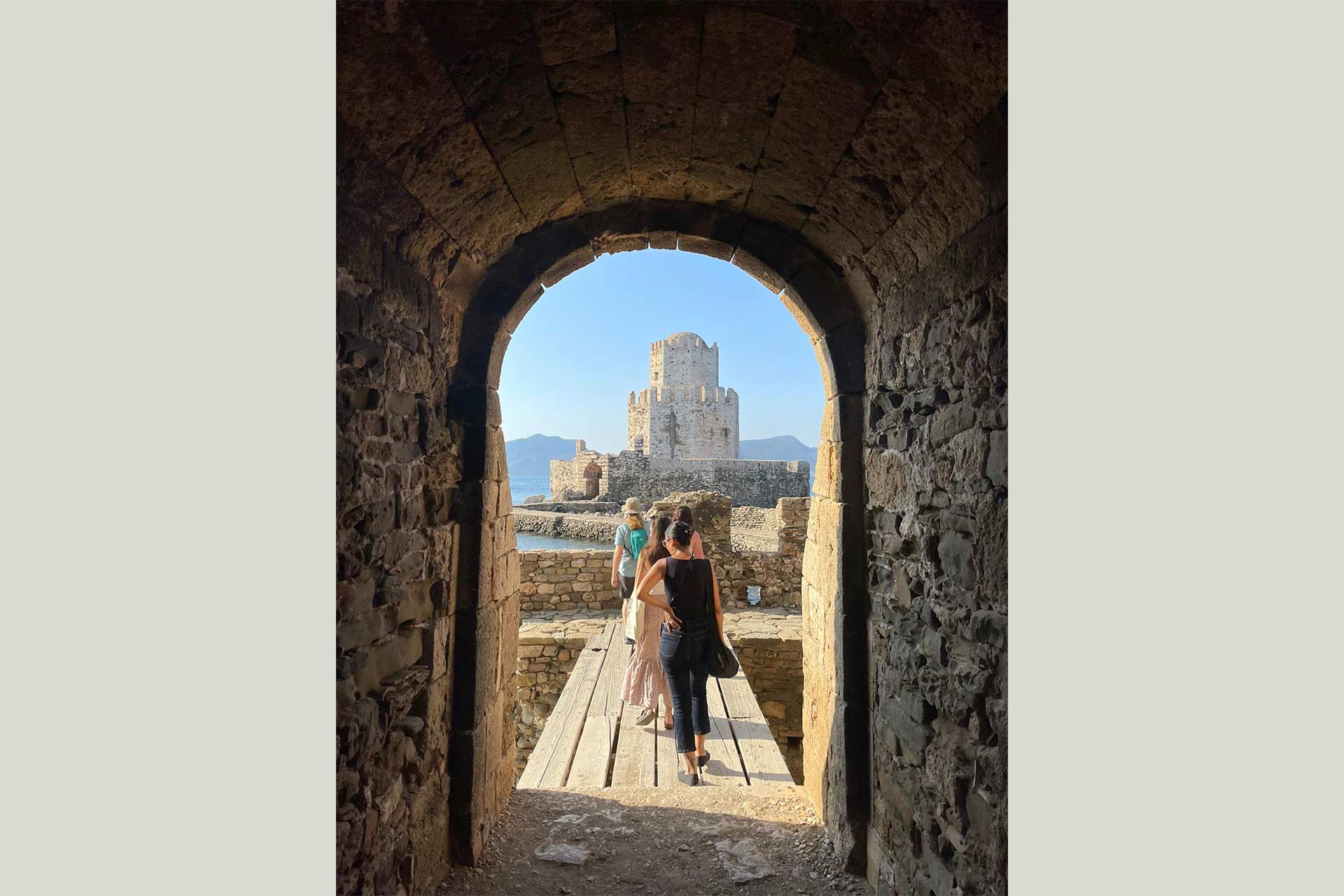 An old stone archway looking over to a large grand ancient greek building.