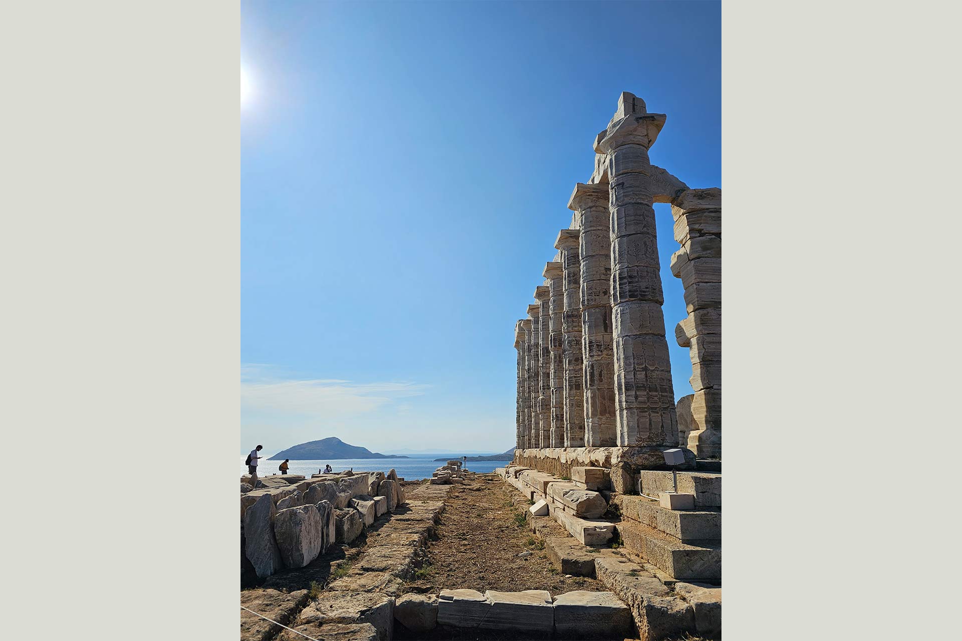 An ancient Greek structure with pillars by the sea, with an island in the background.