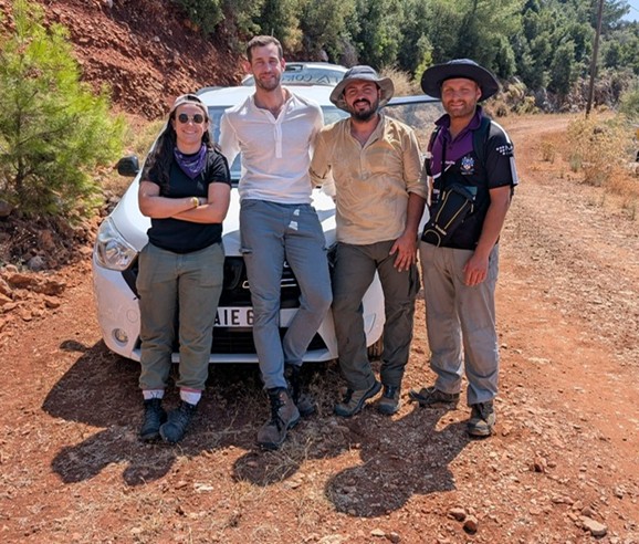 Four people standing together outside in front of a white car.