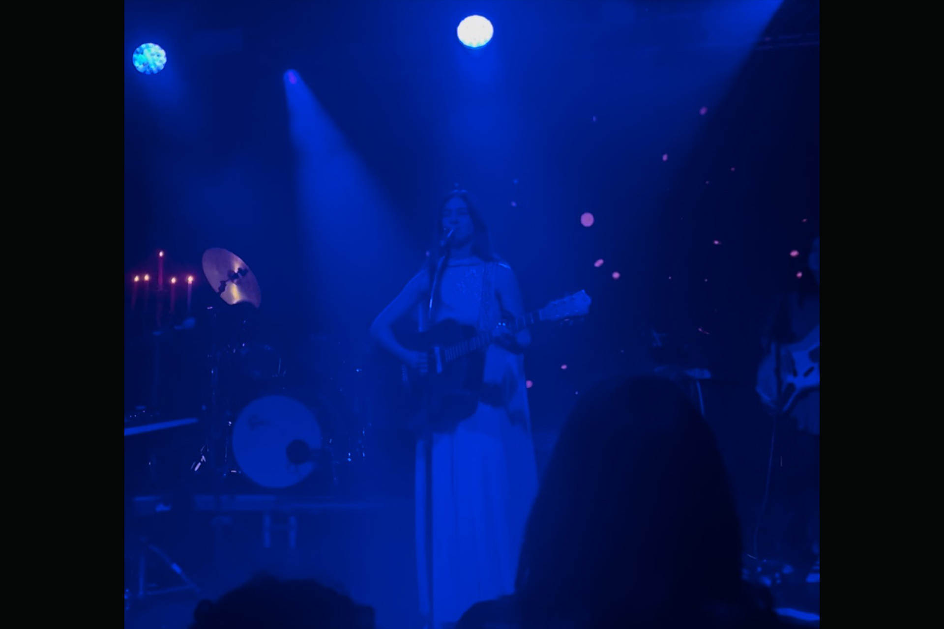 A band on stage lit with a soft blue light, the lead singer playing a guitar and singing into a microphone.