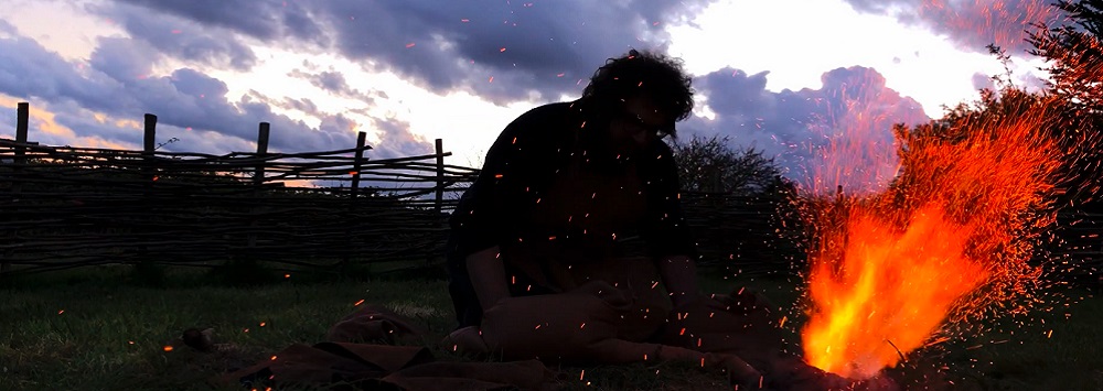 Silhouette of someone lighting a fire against a twighlight sky. The features of the person are not visible.
