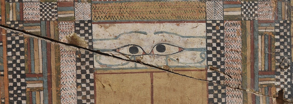 Detail of the front side of a coffin featuring ancient Egyptian illustrated eyes and colourful patterns
