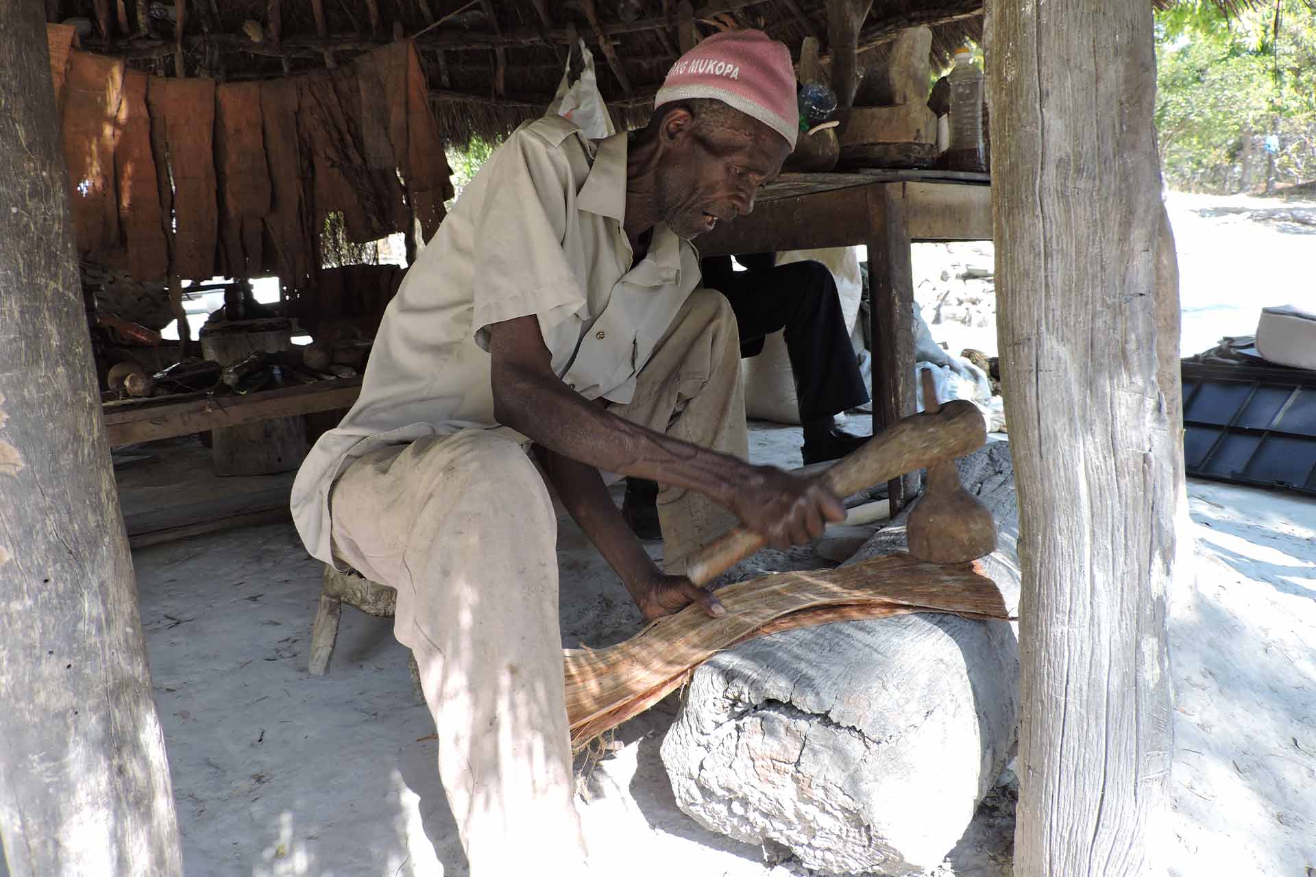 A man using a wood mallet on fabric against a log work surface