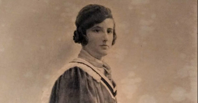 Sepia photograph of a woman wearing a formal graduation gown and holding hat