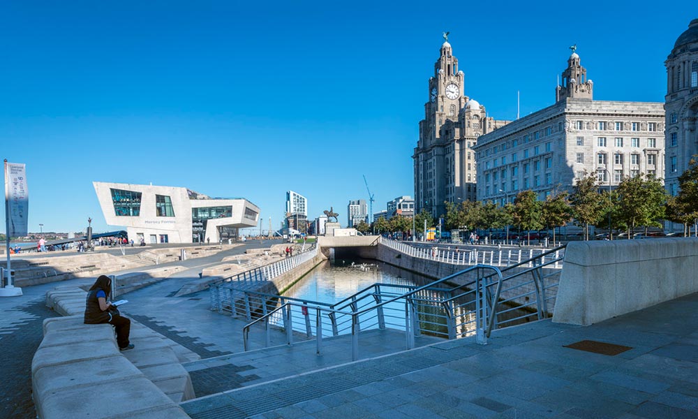 Person sitting alone by a canal in front of the Liver Buildings