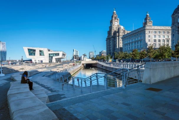 Person sitting alone by a canal in front of the Liver Buildings