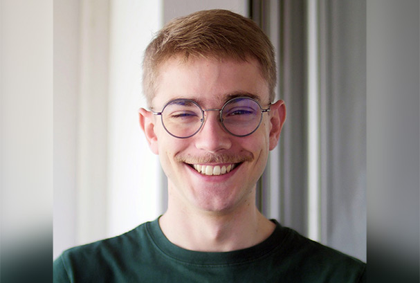 Head and Shoulders of a young man with short cropped ginger hair and moustache. He is wearing round glasses