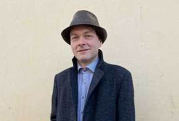 Middle aged man wearing a Dark blue coat, blue shirt and grey hat