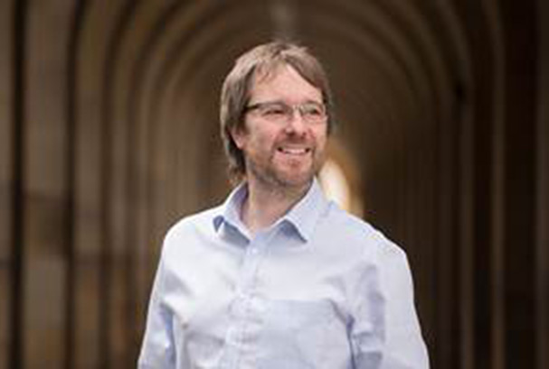 White man with light brown hair and beard, wearing a grey shirt, standing in a cathedral