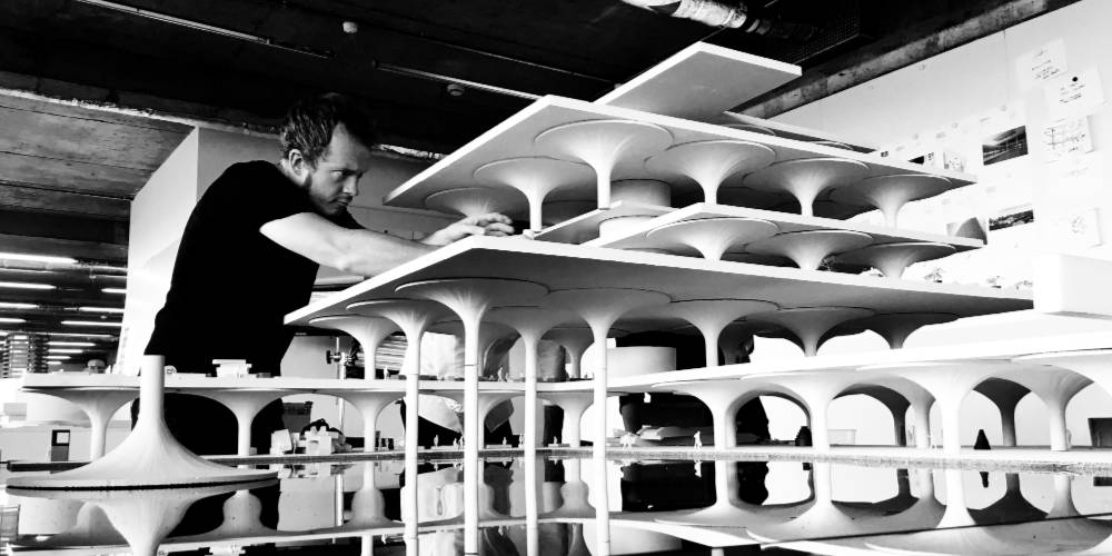 WHite man with short hair and beard building a model structure consisting of stacked ceramic columns each flailing widely at the top