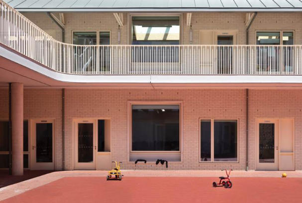 Atrium space in a School with pink and white walls and pink floor. Two children's tricycles sit in the middle of the space along with a ball and discarded jumpers