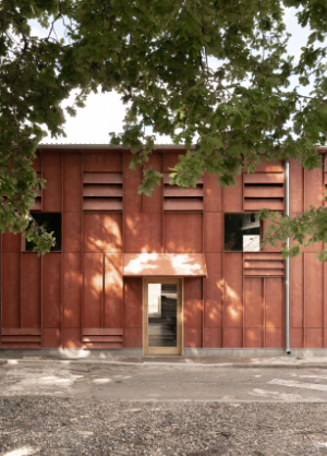 Rust coloured building with prominent vertical ribs and vents, framed by foliage