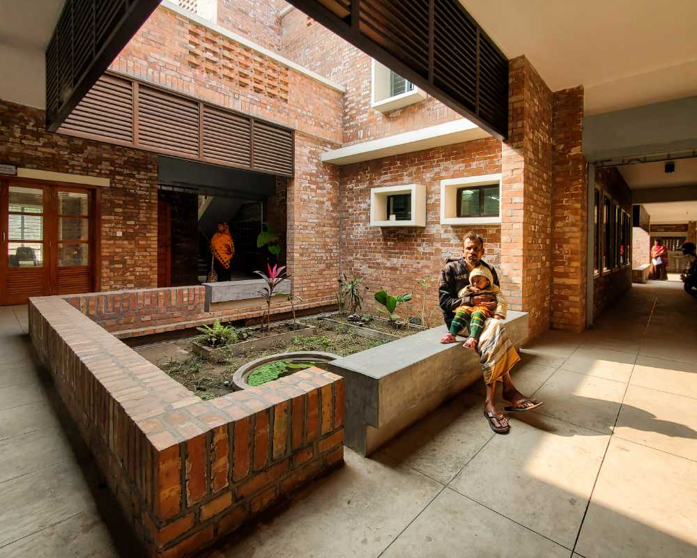 Brick built courtyard. On a wall a man sits holding a baby.
