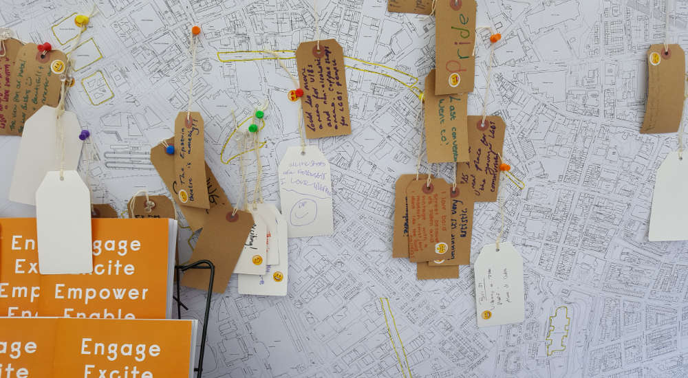 Map of an urban area, pins are placed at various points with cardboard luggage tags hanging from them.