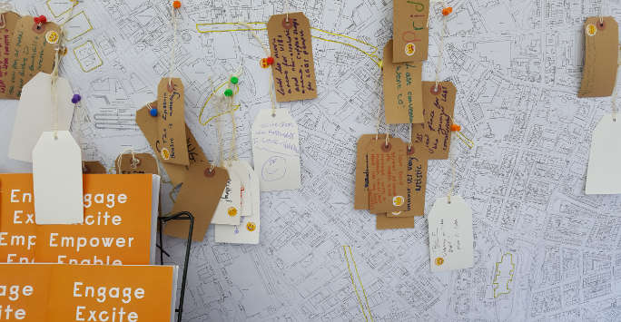 Map of an urban area, pins are placed at various points with cardboard luggage tags hanging from them.