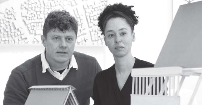 A man and a woman standing and looking at building models, behind them is a relief model of a site plan.