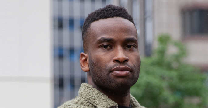 Young man with short cropped afro hair wearing a fluffy sage shirt.