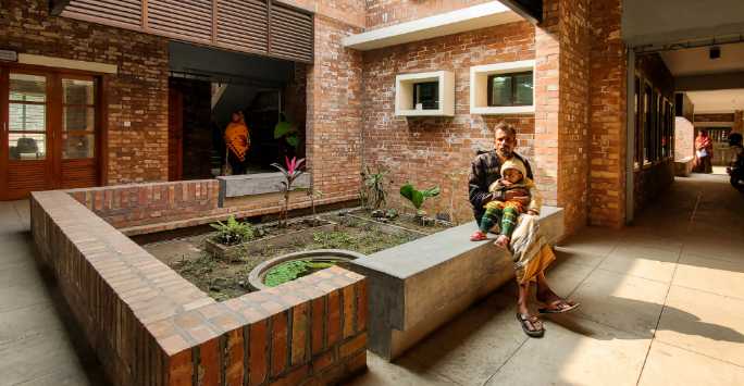 Brick built courtyard. On a wall a man sits holding a baby.